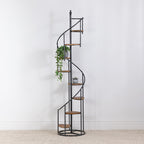 Black spiral display shelf styled with trailing greenery and a small potted succulent against a white wall.
