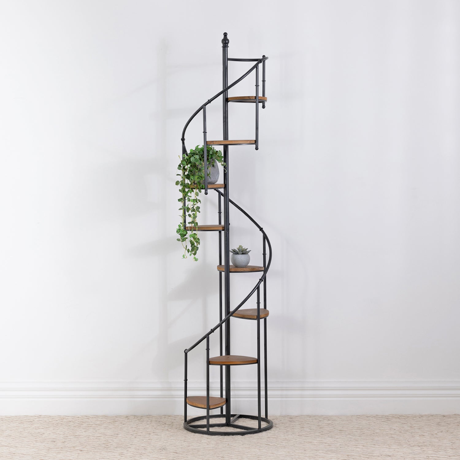 Black spiral display shelf styled with trailing greenery and a small potted succulent against a white wall.