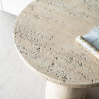 Close-up of the Design Republique Natural Cement Round Side Table showcasing its textured travertine-look tabletop with a magazine resting on the surface.