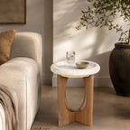Amparo Fleur stone side table styled beside a neutral sofa with a glass and bowl on top.