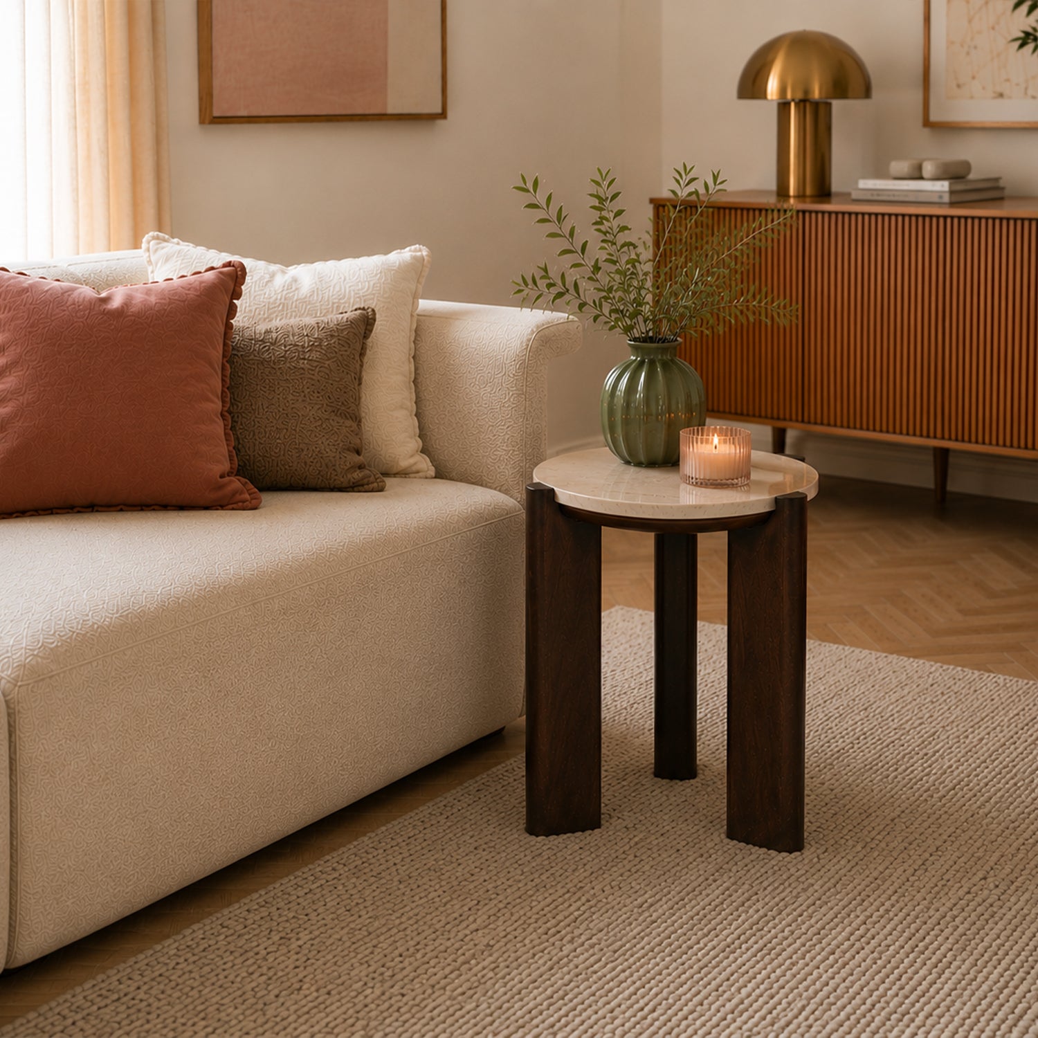 **Round side table with a cream marble top and chunky dark brown timber legs styled beside a cream sofa, decorated with a green vase and lit candle in a warm contemporary living room.**
