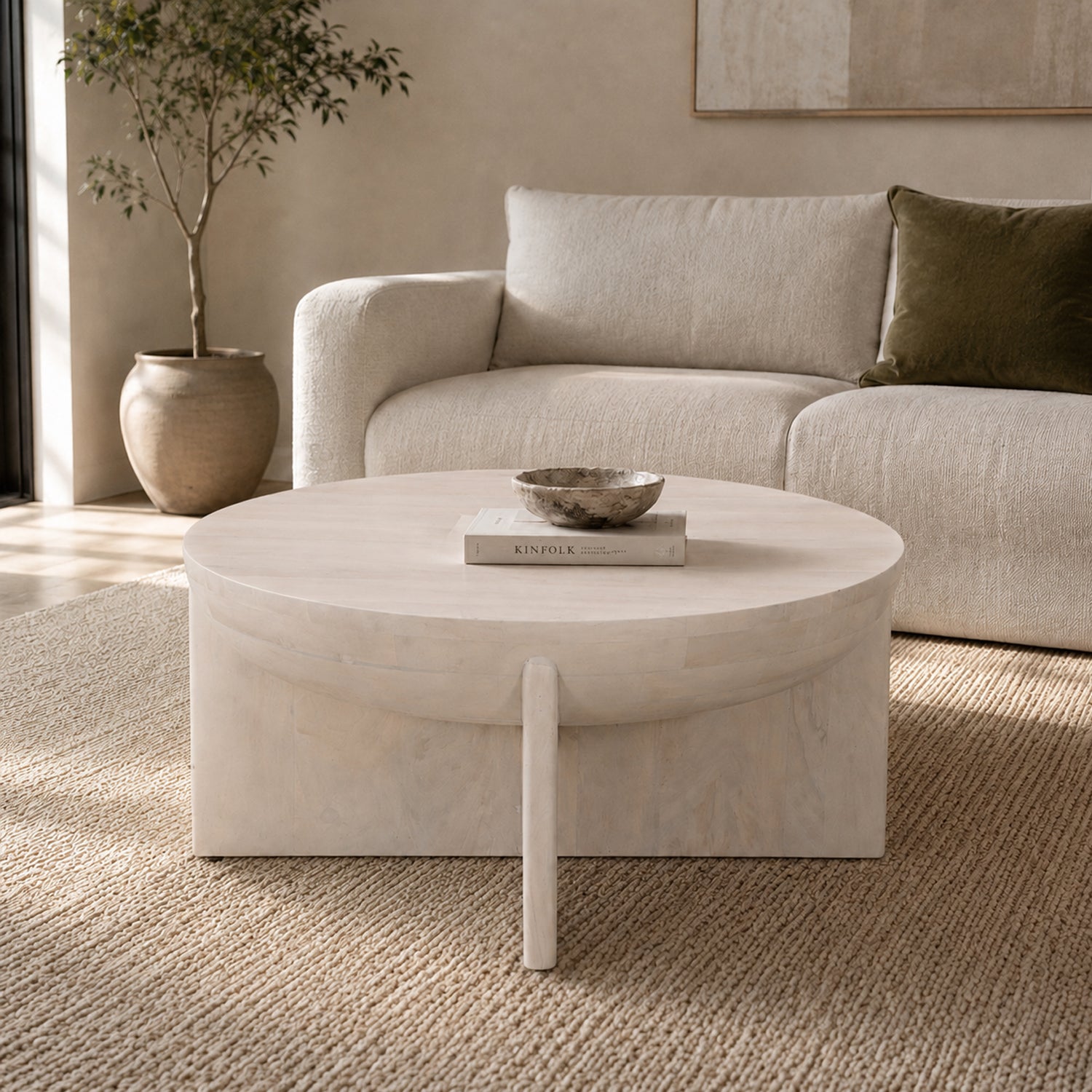 Amparo mango wood coffee table in white wood styled in a neutral living room, featuring a round tabletop with a bowl and book on top.