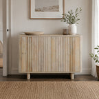 Natural mango wood sideboard with vertical slatted doors styled in a bright contemporary living space with decorative accessories, framed artwork, greenery, and a woven rug.