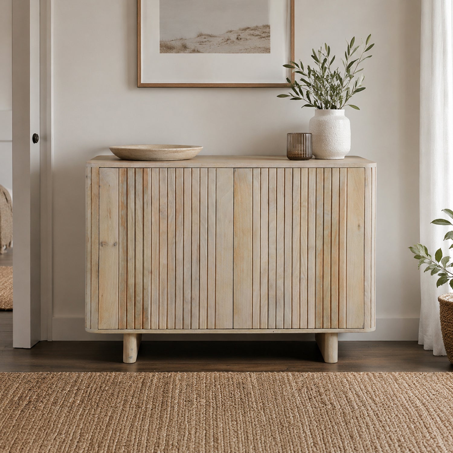 Natural mango wood sideboard with vertical slatted doors styled in a bright contemporary living space with decorative accessories, framed artwork, greenery, and a woven rug.