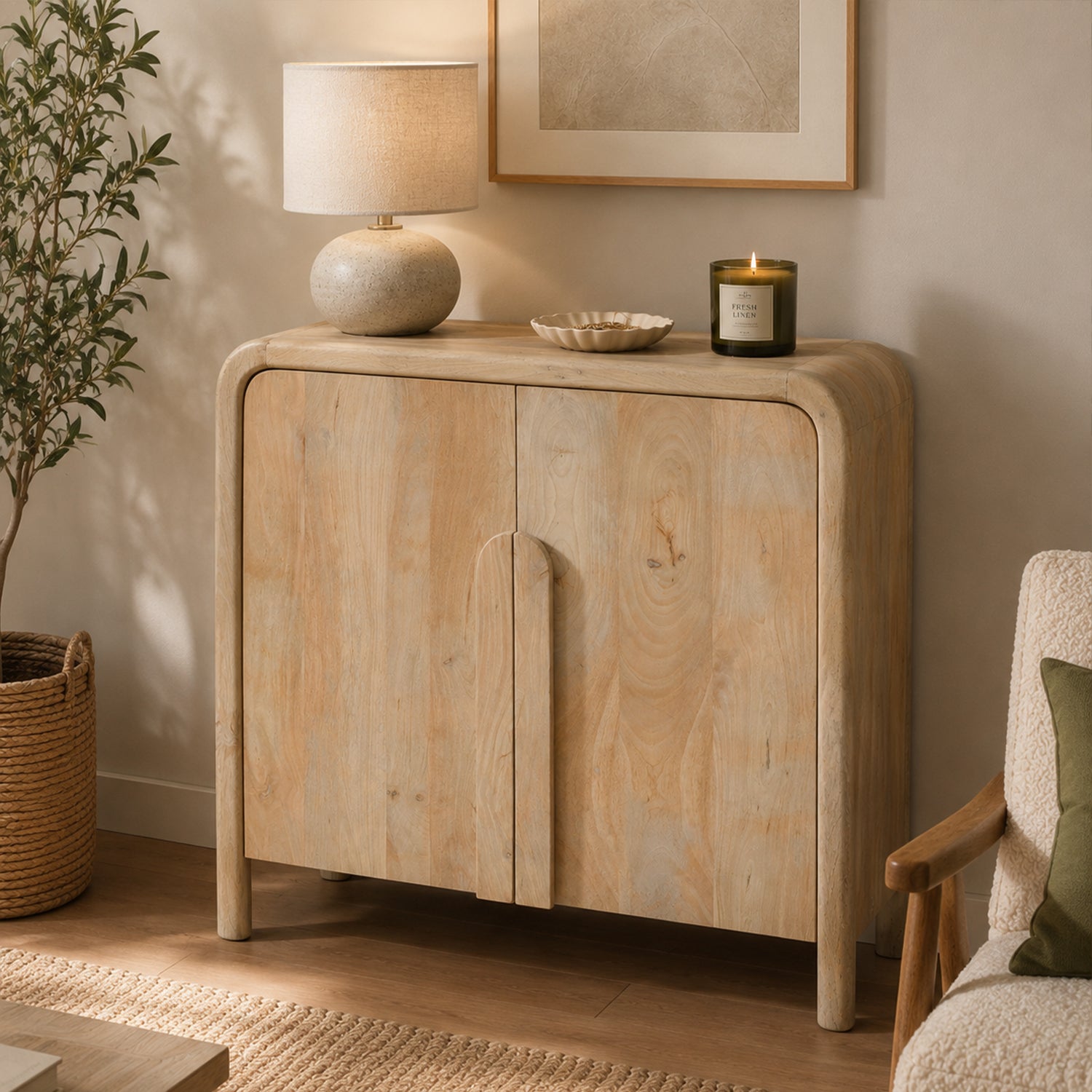 Mango Shona sideboard in natural mango wood with rounded edges and double doors, styled in a contemporary living room with a table lamp, candle, decorative tray, framed artwork, woven basket, and indoor plant.