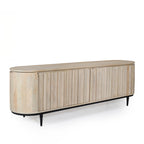 Angled view of the natural mango wood entertainment unit showcasing the fluted sliding doors, rounded profile, and black metal legs.