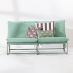 A two-seat cushioned outdoor sofa with a slim green metal frame and green cushions and 3 decorative printed cushions set against a clean white background.