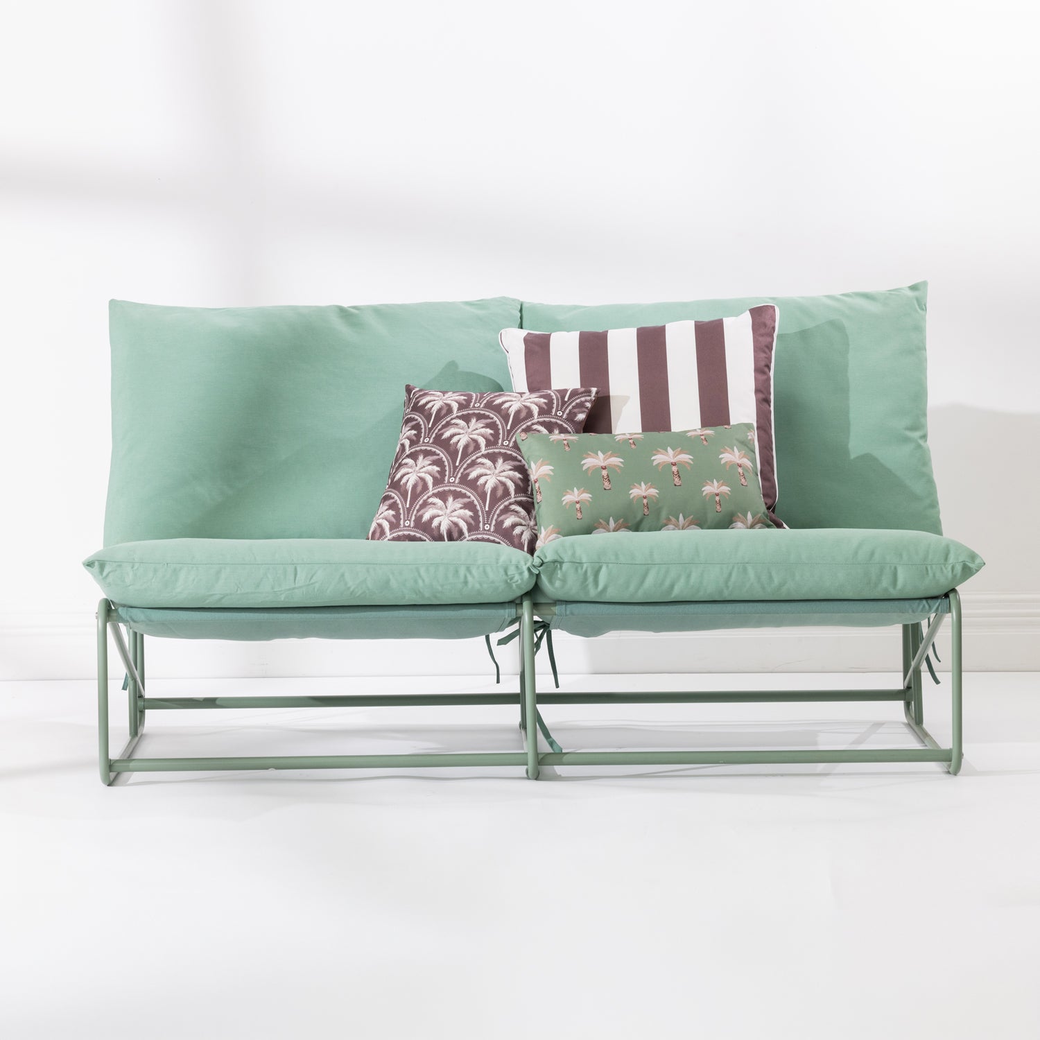 A two-seat cushioned outdoor sofa with a slim green metal frame and green cushions and 3 decorative printed cushions set against a clean white background.