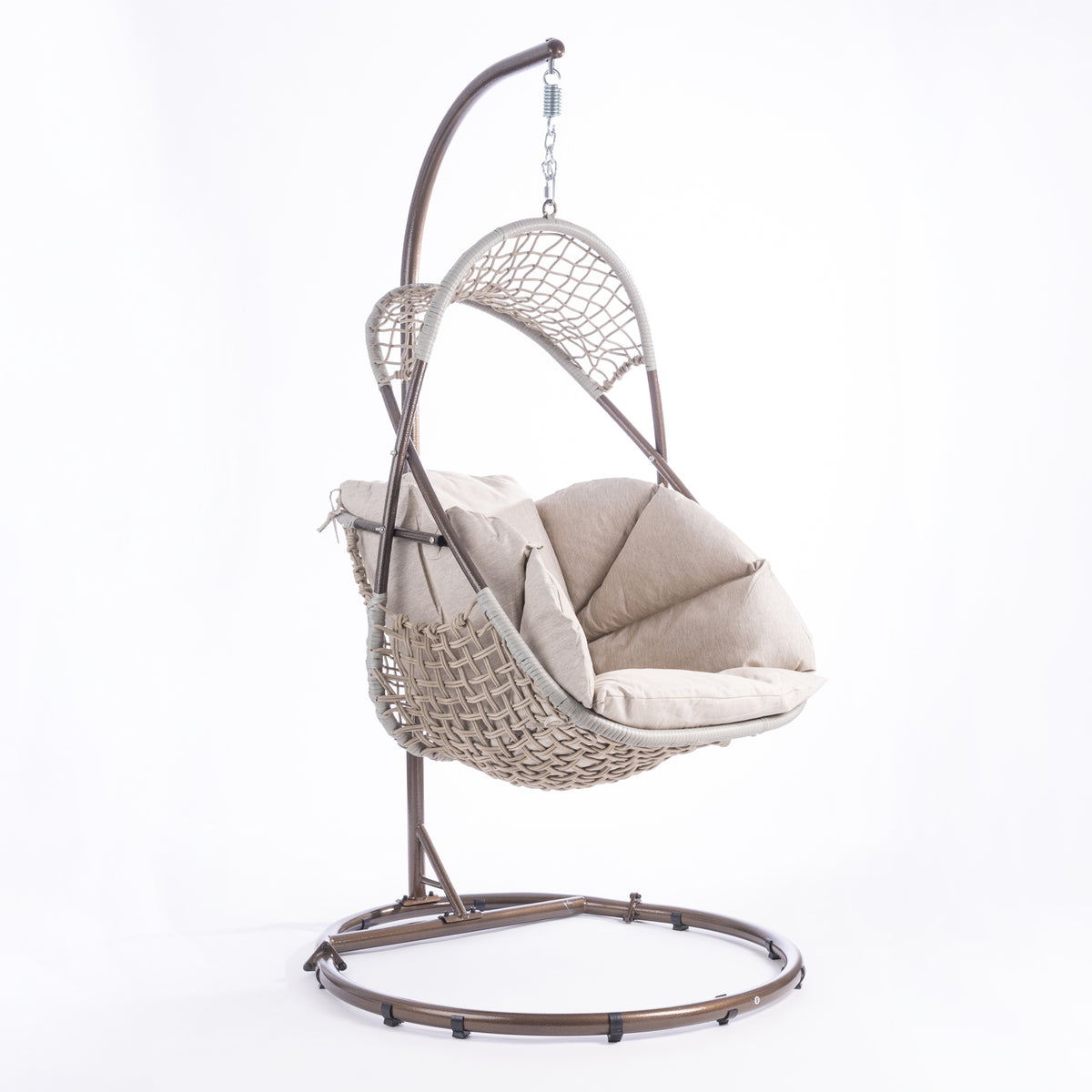 A hanging egg chair with a woven wicker body, beige cushions, and a dark metal stand, photographed in a bright white studio setting.