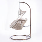 A hanging egg chair with a woven wicker body, beige cushions, and a dark metal stand, photographed in a bright white studio setting.