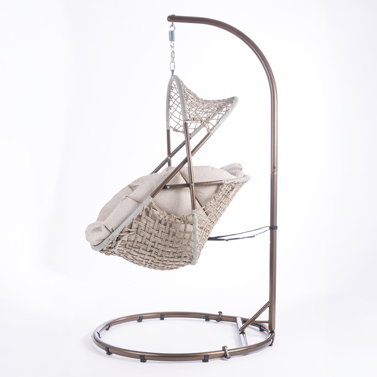 A hanging egg chair with a woven wicker body, beige cushions, and a dark metal stand, photographed in a bright white studio setting.