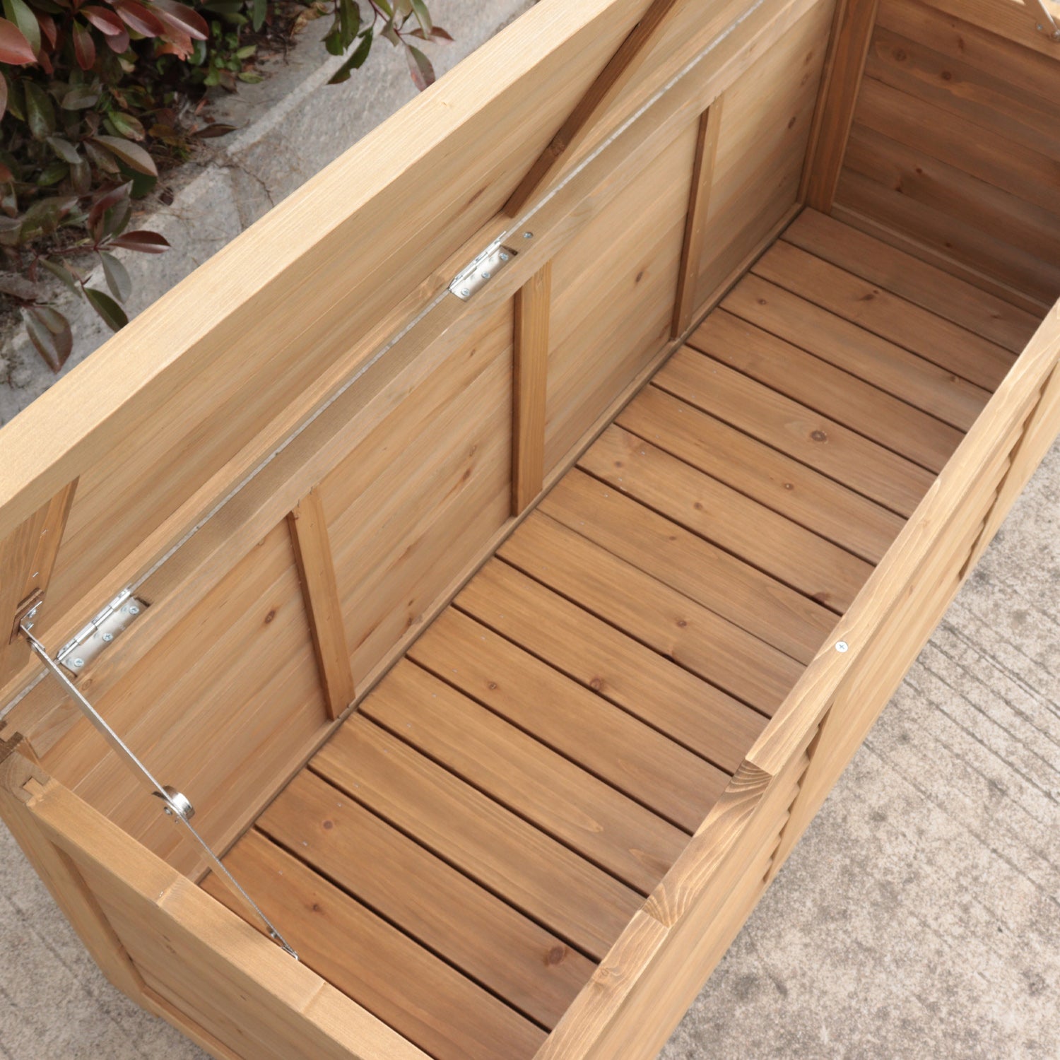 A wooden garden storage bin with a slatted wooden base and a clear plastic lid supported by metal hinges and cables, shown outdoors on a concrete surface.
