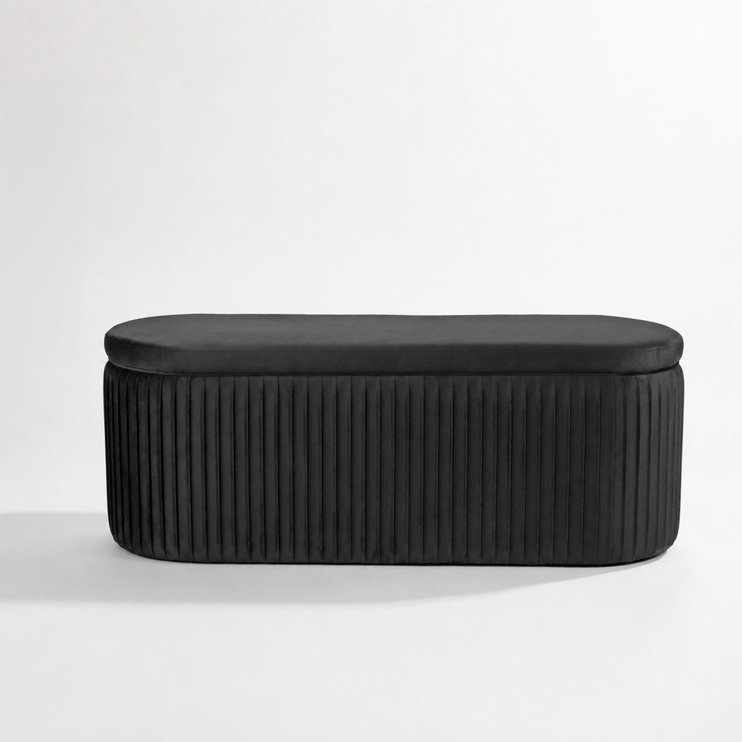 Black pleated velvet storage bench with a smooth upholstered lid, rounded corners, and vertical channel-stitched sides, displayed against a clean white background.