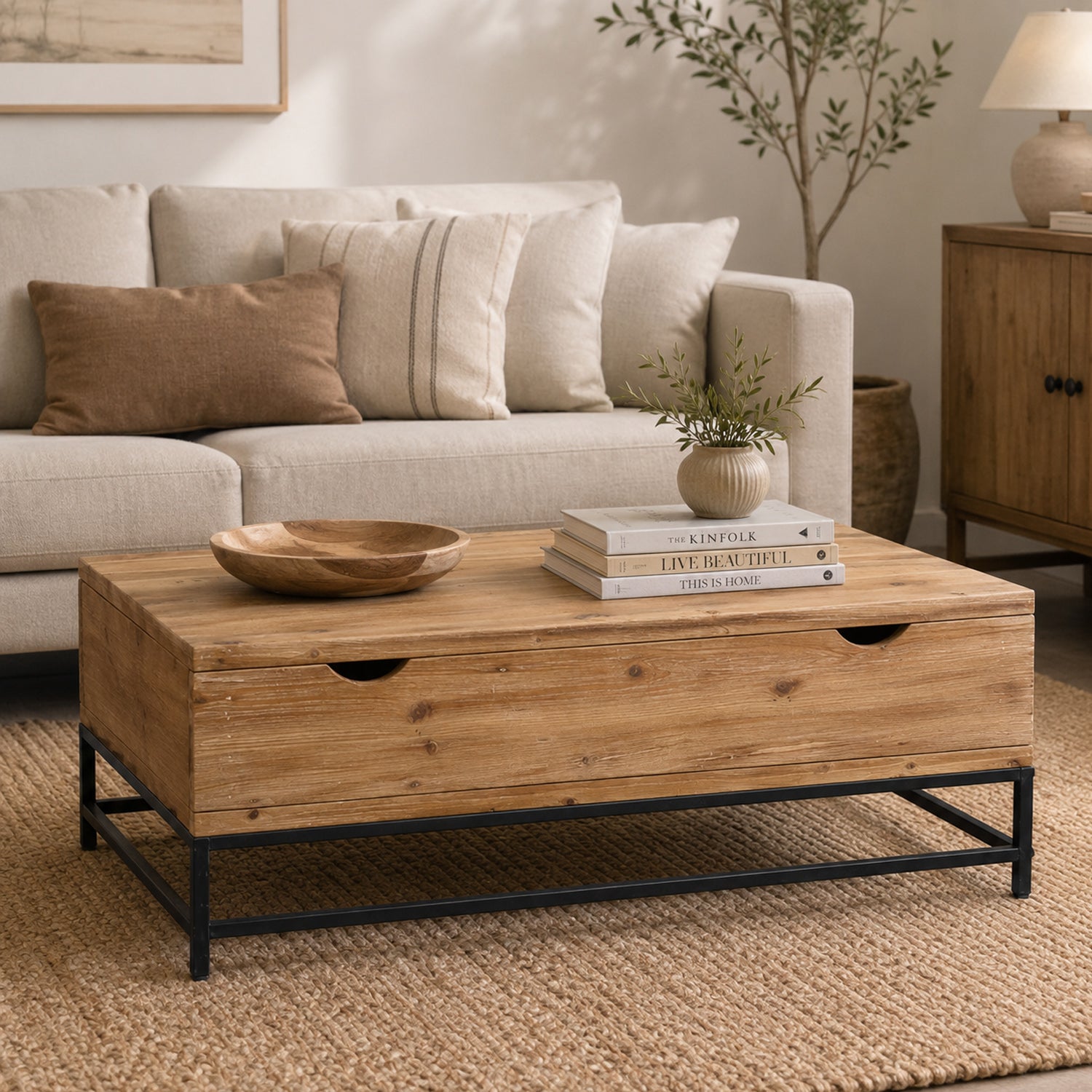 A rustic wooden coffee table with built-in storage and a black metal frame is styled with decorative accents in a warm, neutral living room.