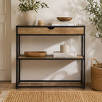 A rustic wood and black metal console table with a single drawer and open shelving is styled with decorative accents to create a warm, contemporary entryway or living space.