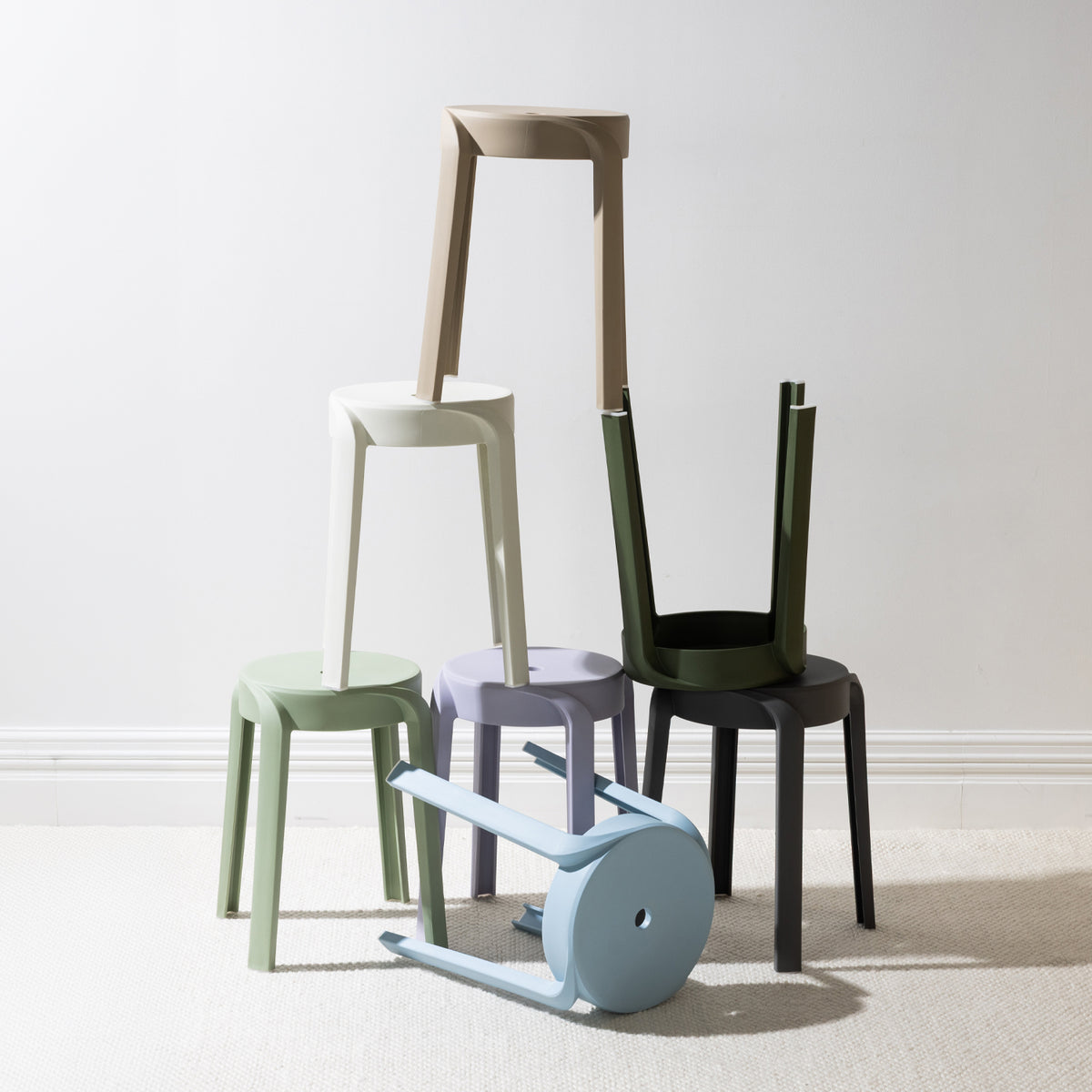 A collection of stackable stools in soft contemporary colours is arranged in an artistic display, highlighting their versatile, space-saving design and modern minimalist style.
