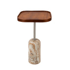 A modern side table featuring a wavy, rounded rectangular wooden top in a warm medium brown finish, supported by a polished silver metal stem and a cylindrical base made of marbled beige and cream stone with brown veining, set against a solid white background.