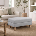 A generously sized neutral ottoman is beautifully styled in a bright, timeless living room, offering versatile comfort as a footrest, extra seating or a stylish coffee table alternative.
