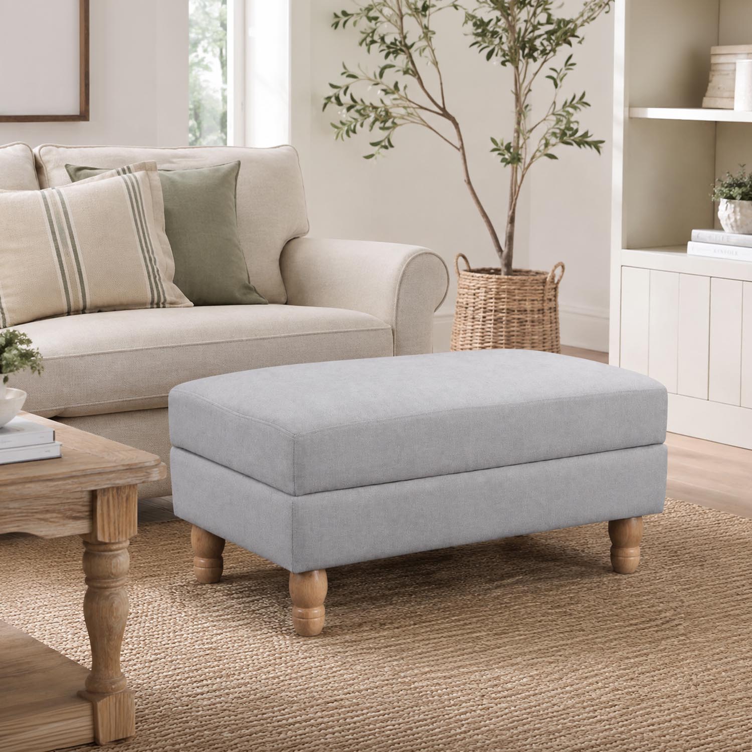 A generously sized neutral ottoman is beautifully styled in a bright, timeless living room, offering versatile comfort as a footrest, extra seating or a stylish coffee table alternative.