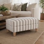 A classic striped ottoman in soft neutral tones is beautifully styled in a warm, inviting living room, offering versatile comfort as a footrest, extra seating or a stylish coffee table alternative.