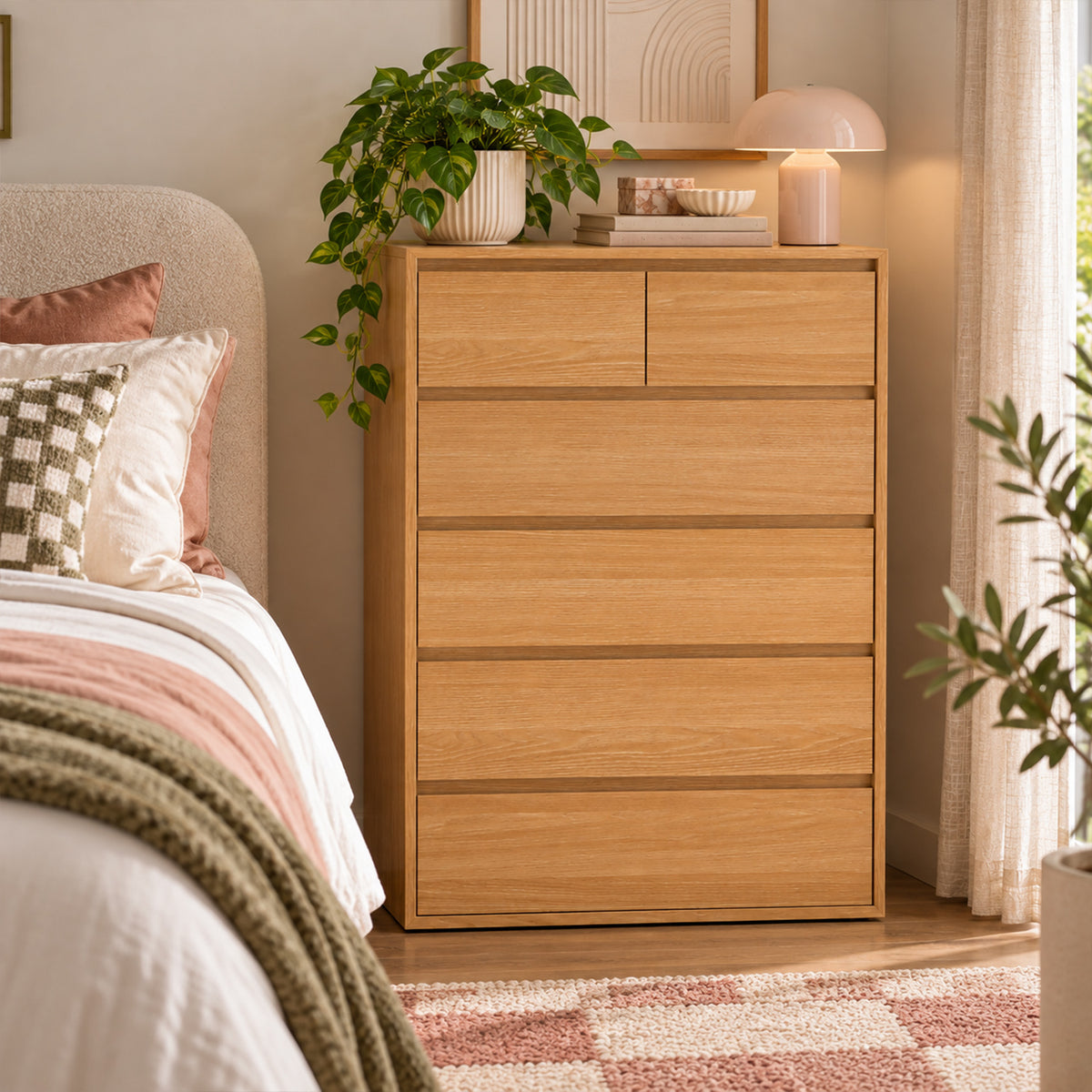 Home Co. Olsen 6 Drawer Tallboy in Natural styled in a warm bedroom setting beside a bed, with a lamp, books and trailing greenery displayed on top.