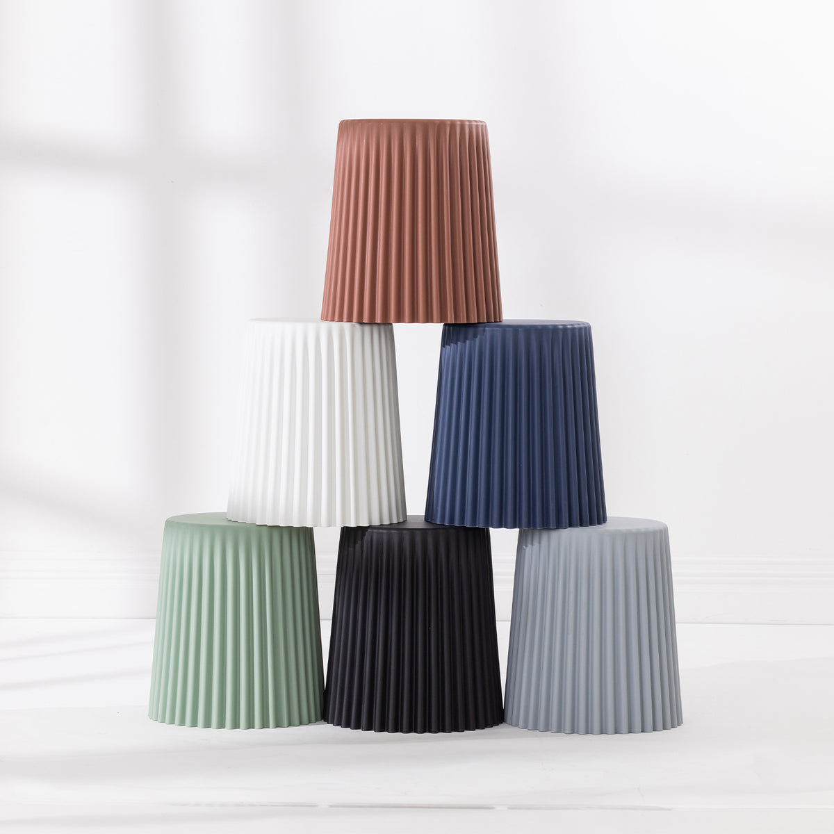 Six fluted side tables stacked together in tan, white, navy, green, black and grey on a white background.