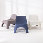 Three moulded plastic chairs in neutral colours: a mocha on the left, a navy blue in the centre, and an cream on the right, arranged on a white floor against a white wall.