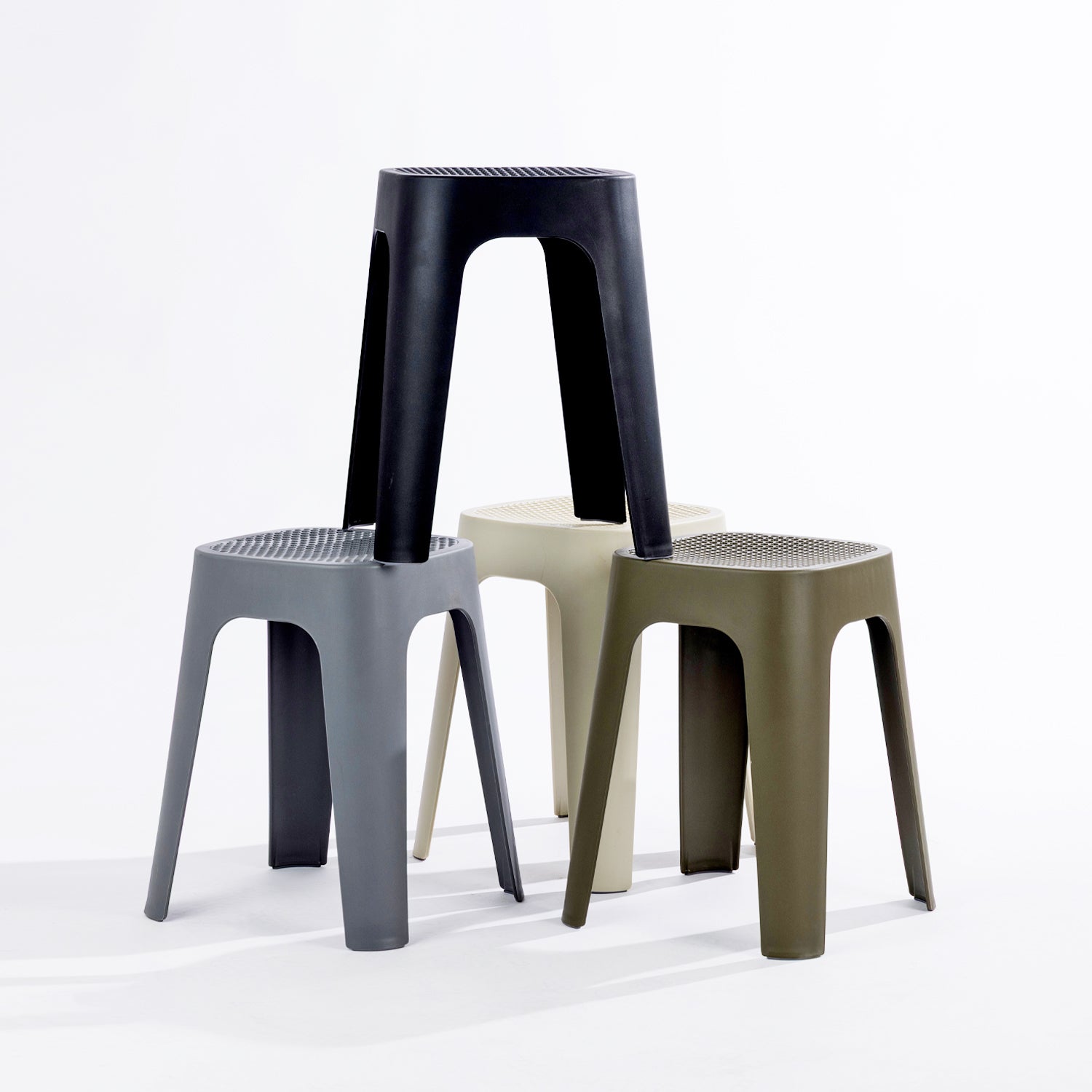Four stools in black, stormy grey, olive & cream, stacked together on a clean white studio background.