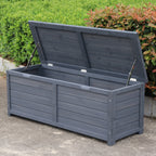 A charcoal wooden storage box with its lid propped open using two metal support rods, set outdoors on a concrete surface with green bushes in the background.