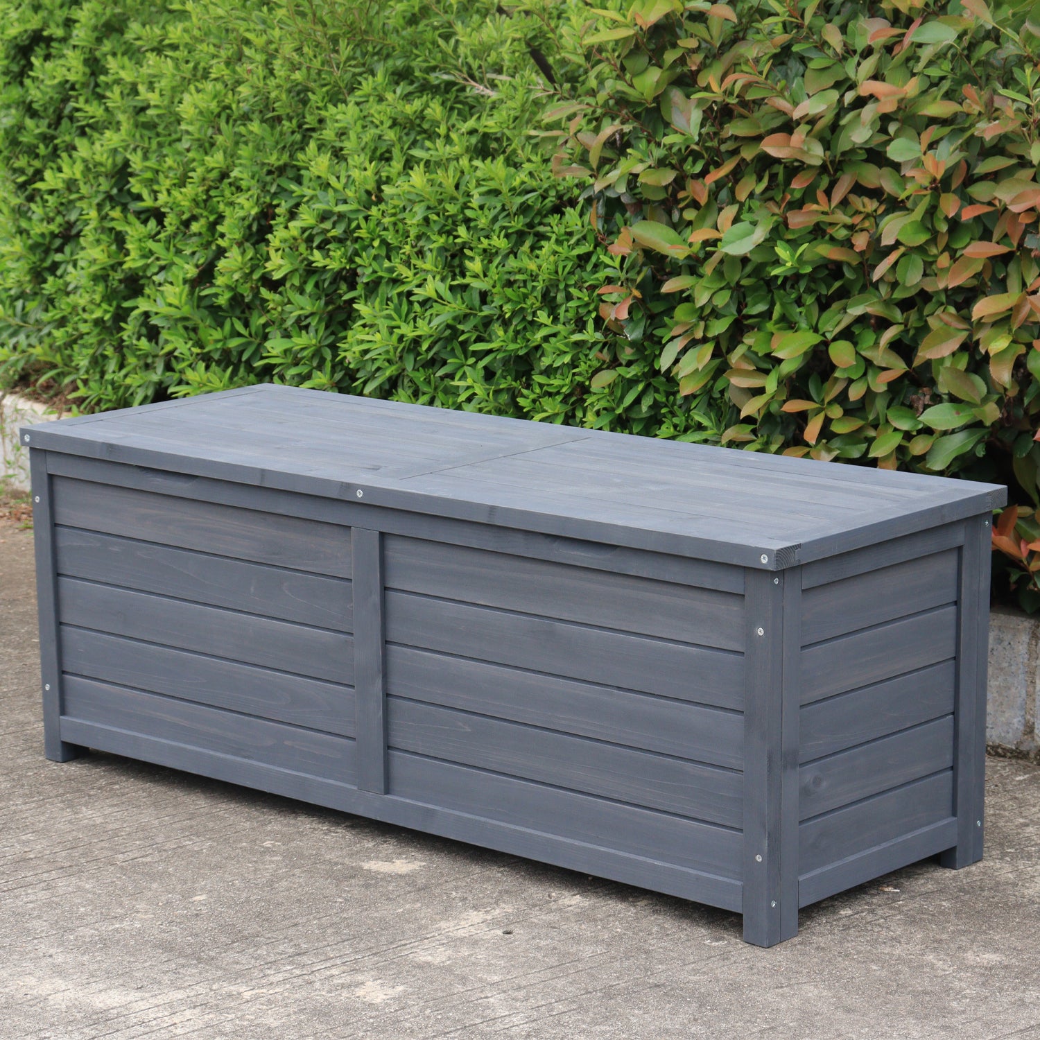 A charcoal wooden storage box, set outdoors on a concrete surface with green bushes in the background.