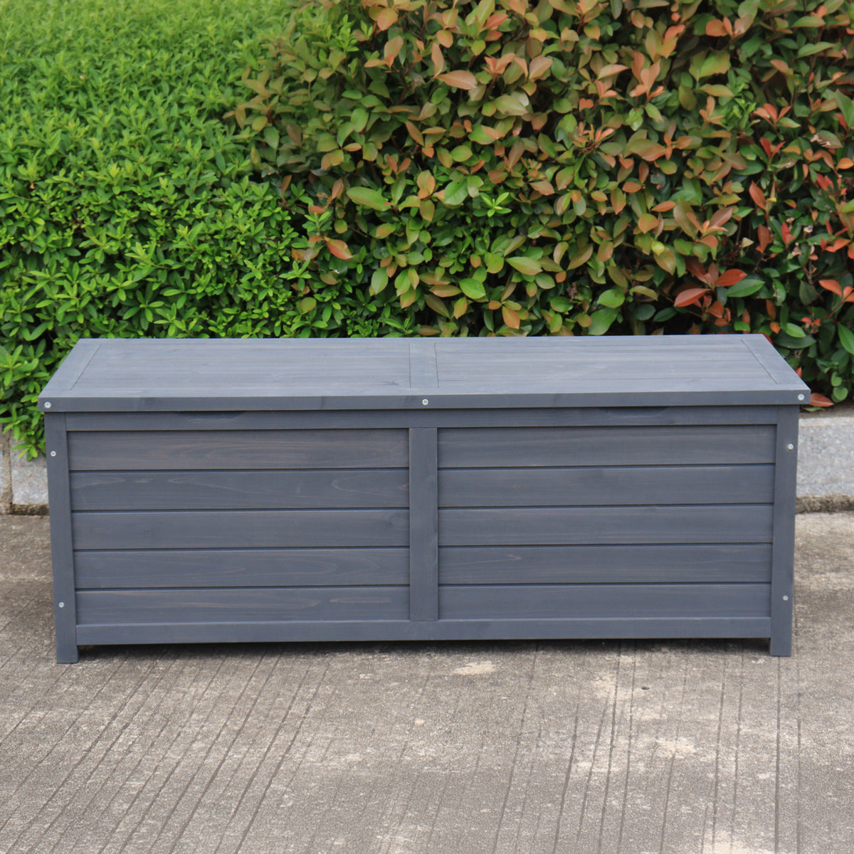 A charcoal wooden storage box set outdoors on a concrete surface with green bushes in the background.