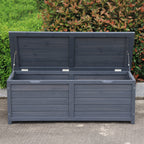 A charcoal wooden storage box with its lid propped open using two metal support rods, set outdoors on a concrete surface with green bushes in the background.