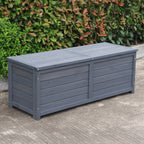 A charcoal wooden storage box, set outdoors on a concrete surface with green bushes in the background.