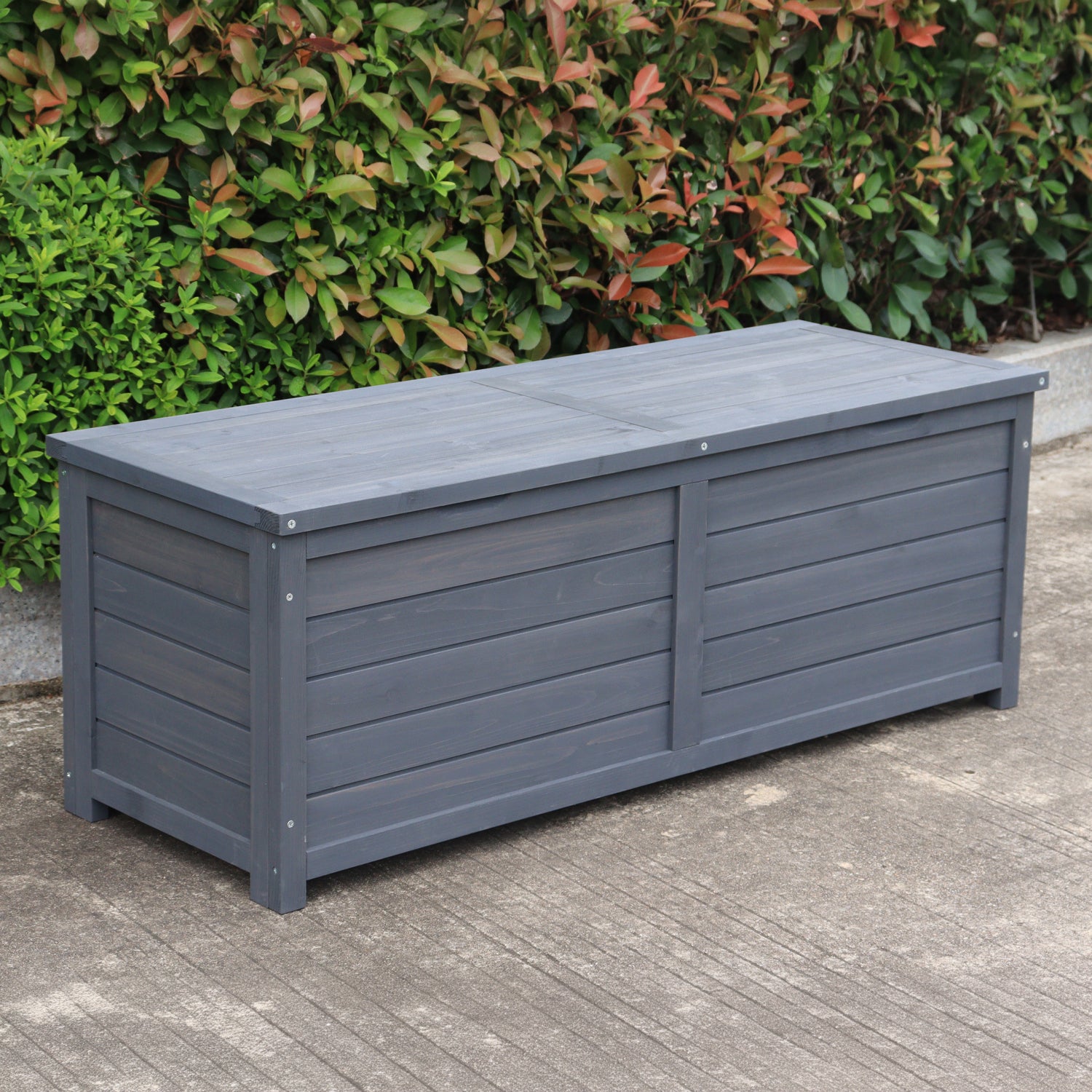 A charcoal wooden storage box, set outdoors on a concrete surface with green bushes in the background.