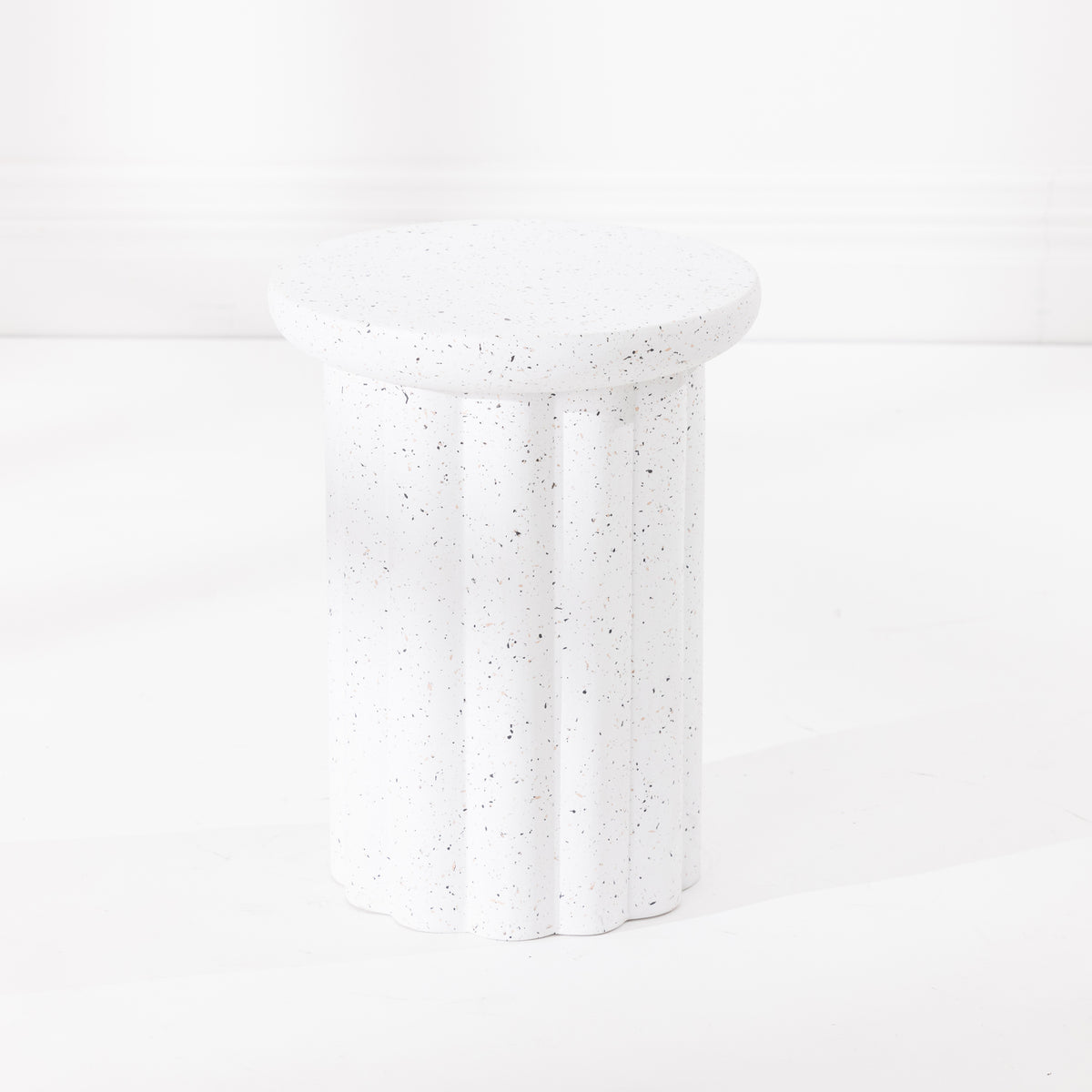 A white fluted pedestal side table with a speckled like finish, set against a clean white background.