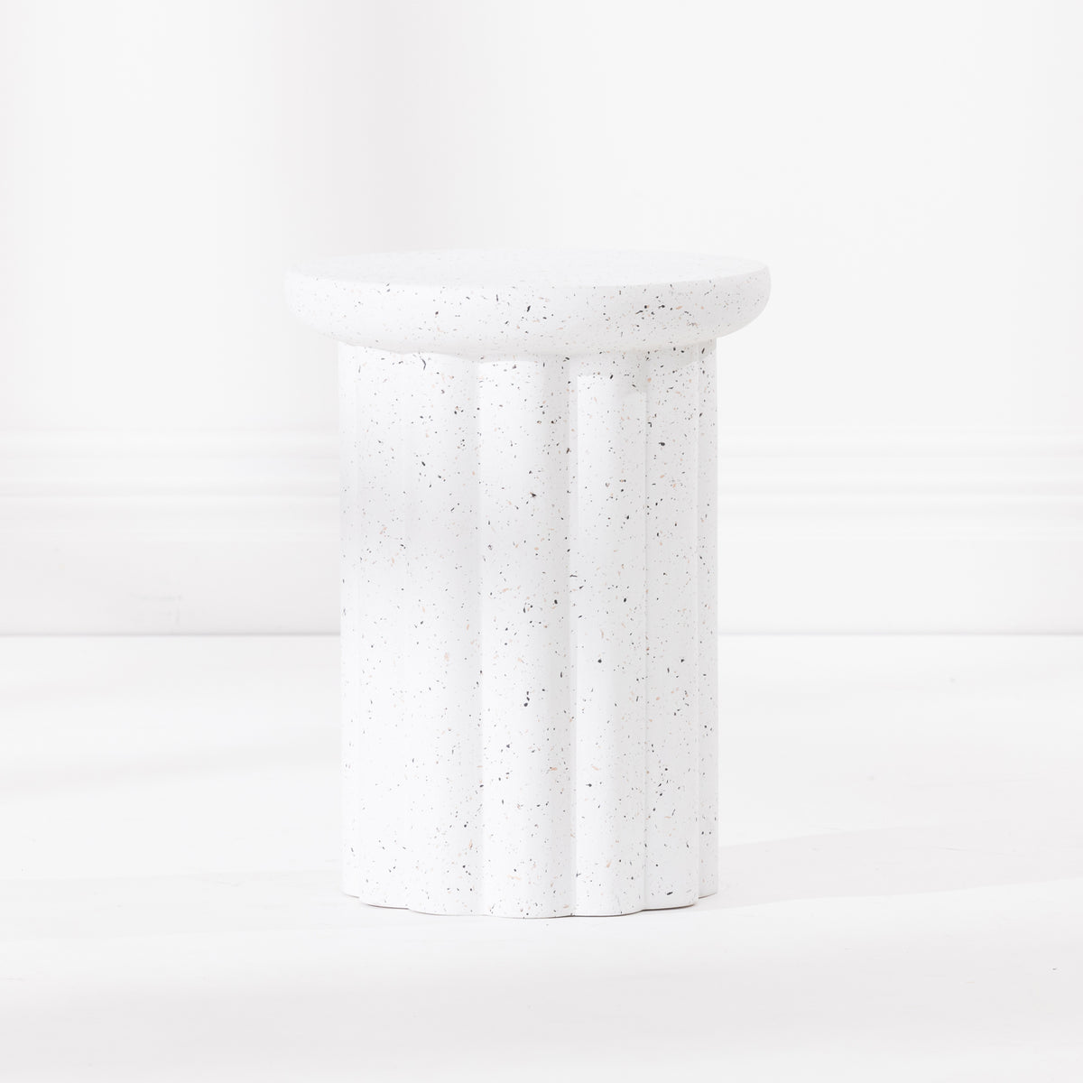 A white fluted pedestal side table with a speckled like finish, set against a clean white background.