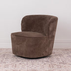 A brown chenille textured fabric swivel armchair with a rounded backrest, shown on a distressed patterned rug against a white wall.