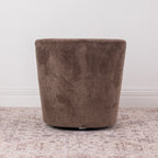 A brown chenille textured fabric swivel armchair with a rounded backrest, shown on a distressed patterned rug against a white wall.