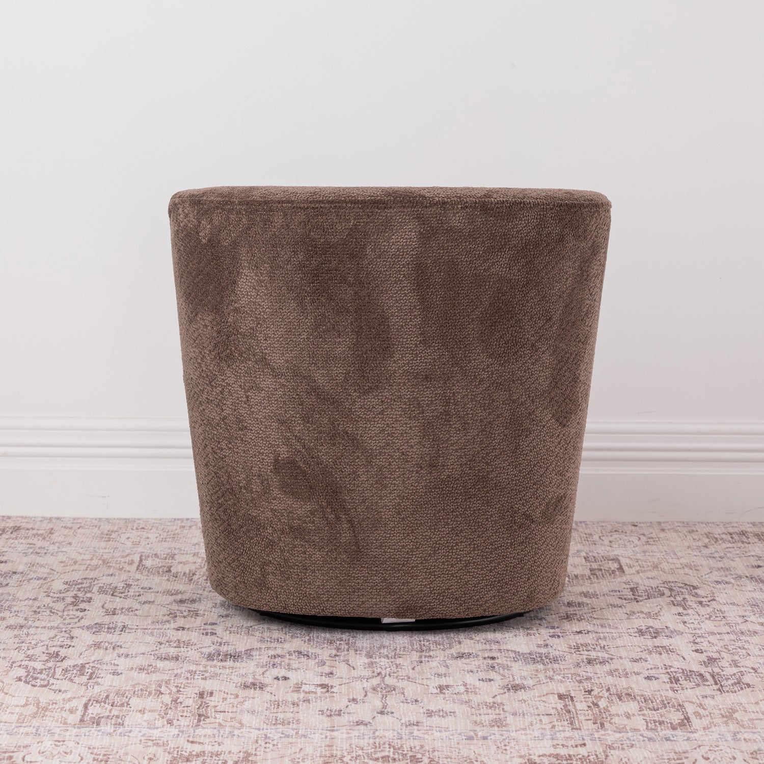 A brown chenille textured fabric swivel armchair with a rounded backrest, shown on a distressed patterned rug against a white wall.