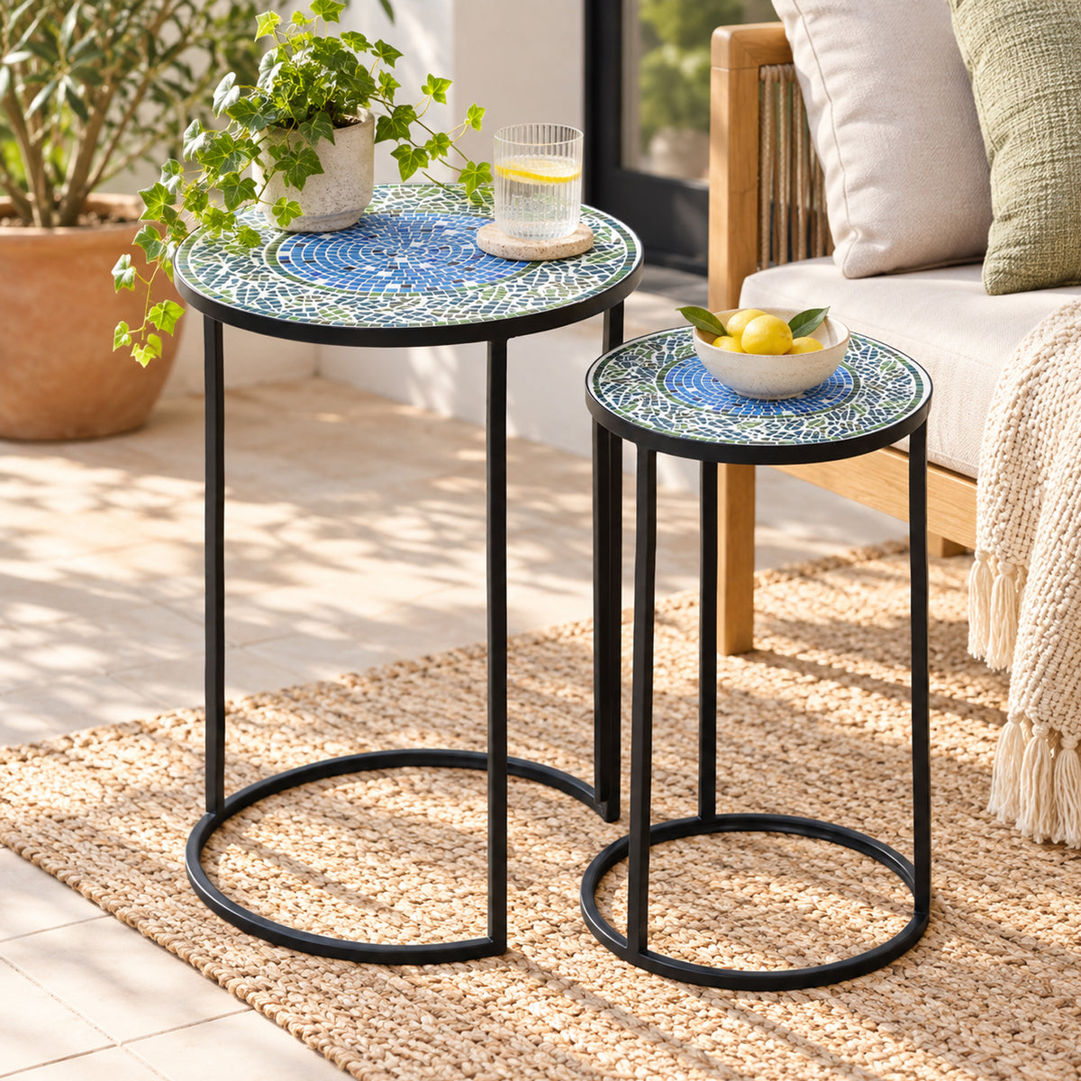 Outsidings Blue Tile Mosaic Side Table Set of 2 styled in a bright living space, featuring blue and green mosaic tabletops, black metal frames, a potted plant, drink and decorative bowl.