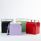 Outsidings Arctic Cooler Box Range displayed in Black, Lilac, Green and Red, featuring matching lids, silver metal carry handles and built-in bottle openers. The Lilac cooler is shown filled with ice, bottled drinks and lemons.