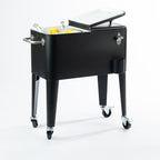 Black 57L cooler box displayed with one lid open, revealing its white insulated interior filled with ice, bottled drinks and fresh lemons. Features a convenient split-lid design, side carry handle and caster wheels.