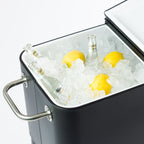 Close-up of the black cooler box's spacious white insulated interior, filled with ice, glass beverage bottles and lemons. The split-lid opening allows convenient access to chilled refreshments.