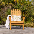 A wooden cape cod-style outdoor chair sits on a weathered deck with tropical palm foliage in the background.