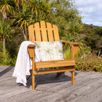 A wooden cape cod-style outdoor chair sits on a weathered deck with tropical palm foliage in the background.