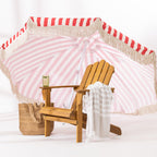 A wooden cape cod chair with a striped fringed towel draped over the arm, set against a red and white striped umbrella backdrop.