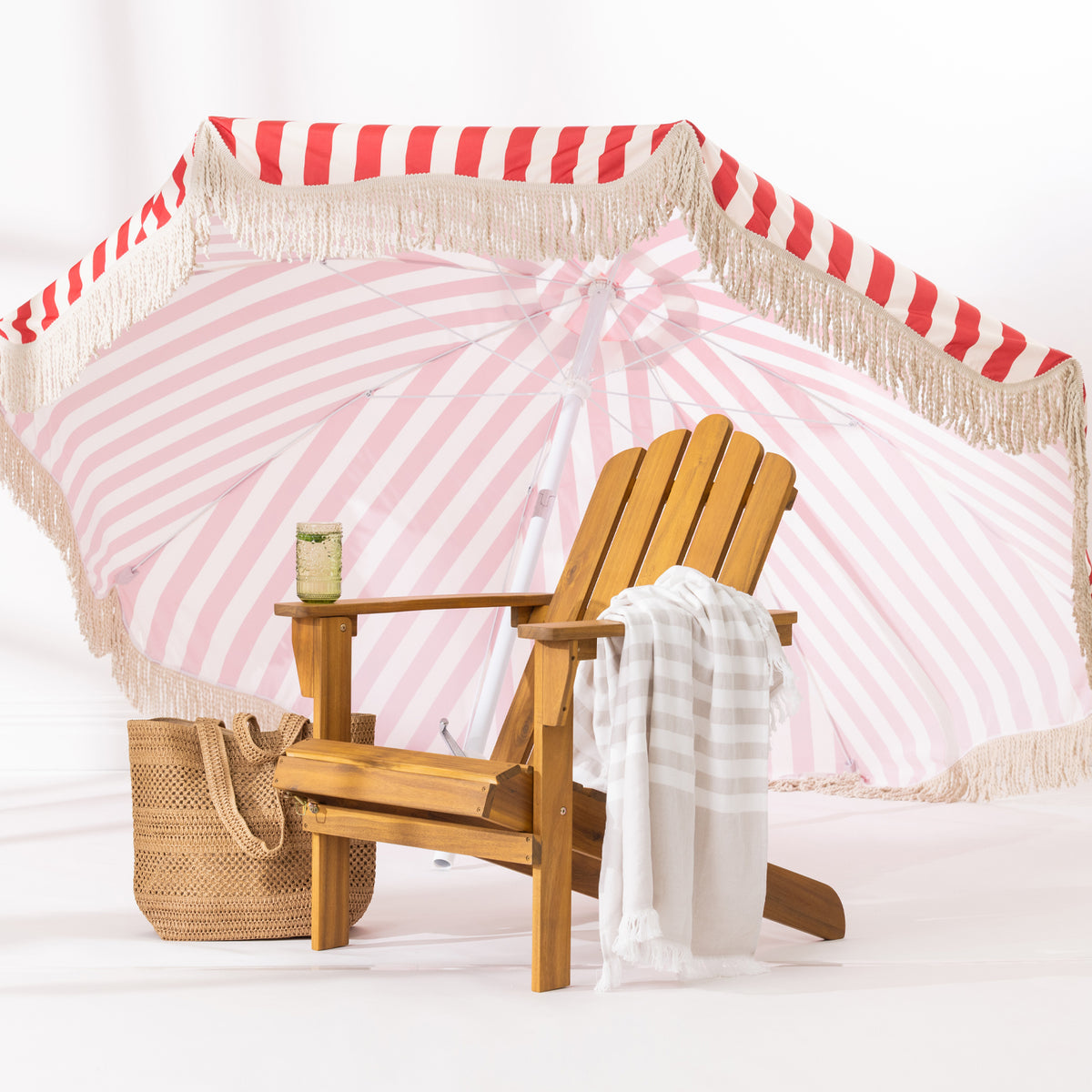 A wooden cape cod chair with a striped fringed towel draped over the arm, set against a red and white striped umbrella backdrop.