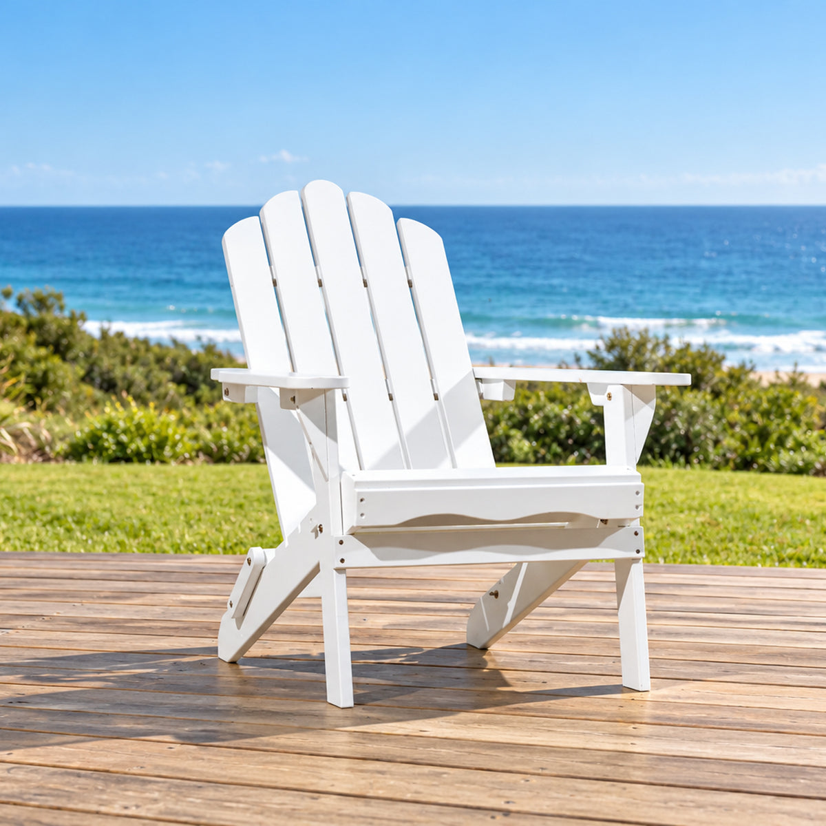 A white outdoor Adirondack chair sits on a wooden deck with a grassy lawn and ocean view in the background.