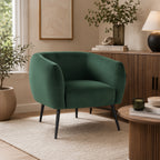 Design Republique Olivia Green Velvet Chair with a curved wraparound silhouette, rich green velvet upholstery and black metal legs, styled in a contemporary living room with warm timber furniture and natural décor.
