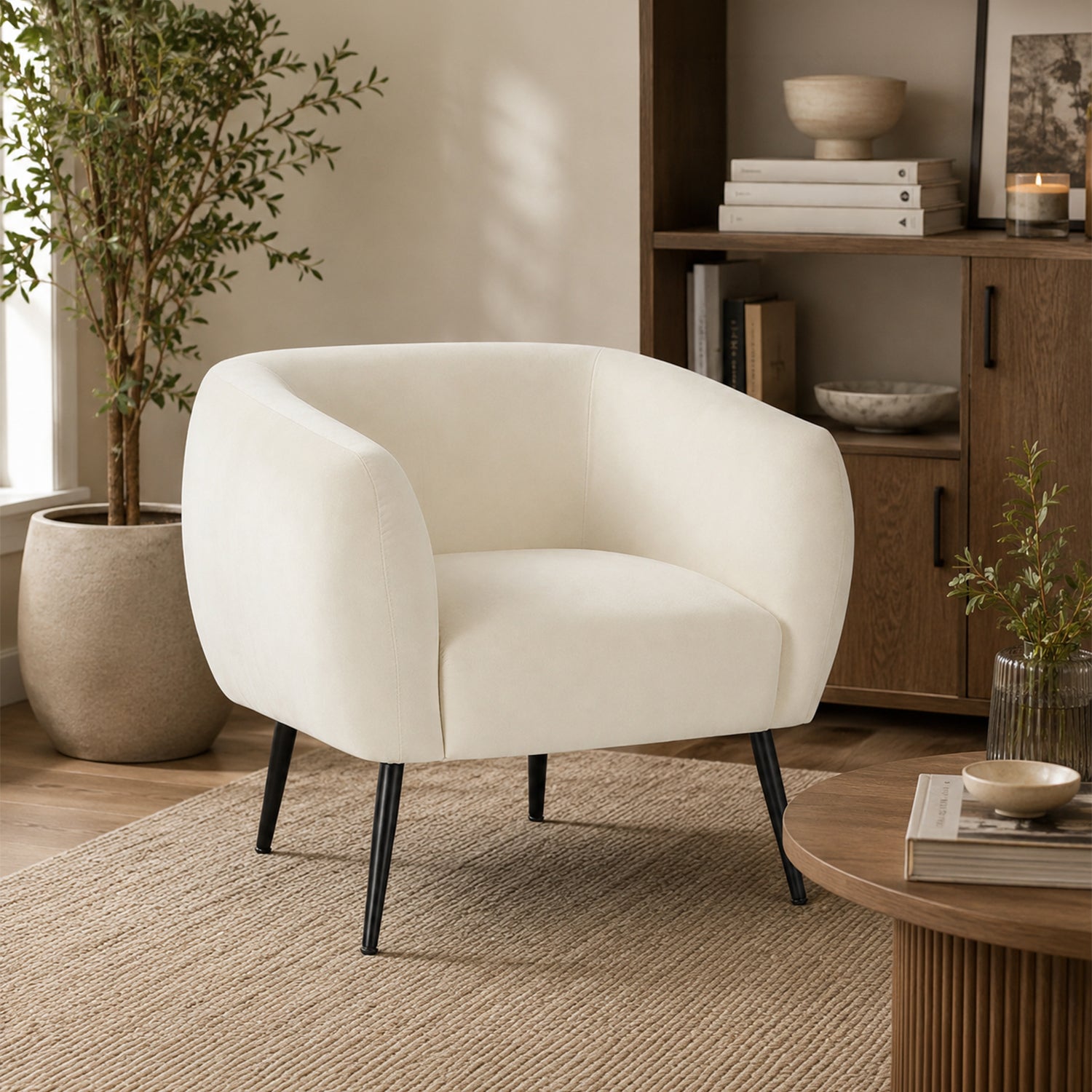 Design Republique Olivia Cream Velvet Chair with a curved wraparound silhouette, soft cream velvet upholstery and black metal legs, styled in a warm contemporary living room with timber furniture and natural décor.